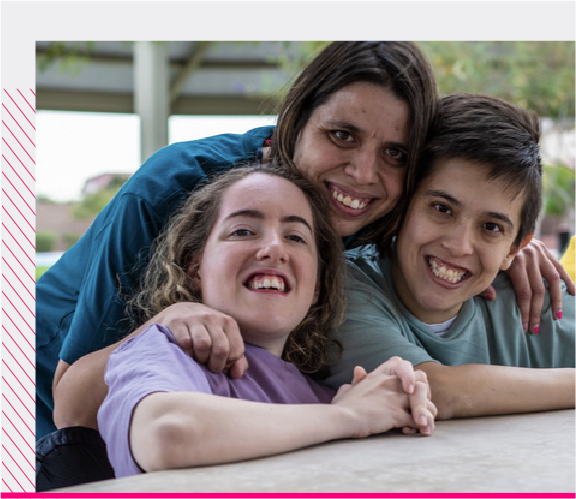3 people with disabilities hugging each other, all smiling in front of the camera